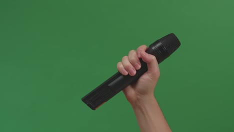 male hand holding microphone against background green screen chroma key. close up mic, interview, live press conference, karaoke, singer performance
