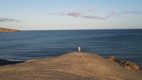 aerial drone shot of a woman standing on a cliff in front of the ocean, canary islands, fuerteventura