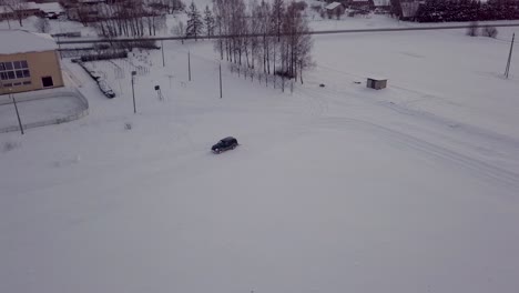 black suv drives around snow field with roll, making track for skiing