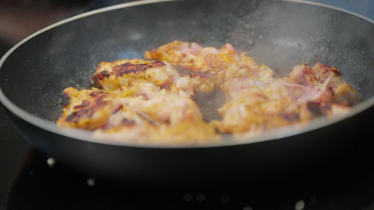 Primo piano di cosce di pollo condite che si rosolano e sfrigolano in una padella su un fornello