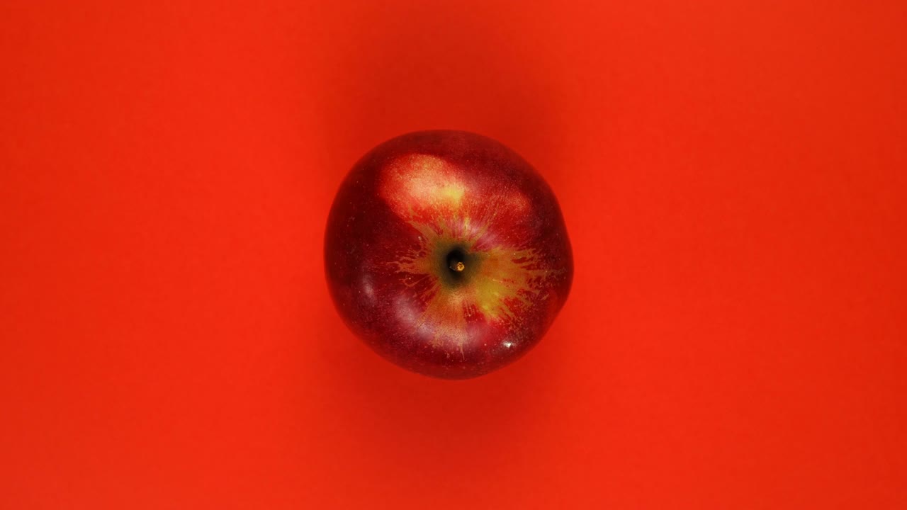 Ripe whole apple fruit rotate around their axis on a red background.