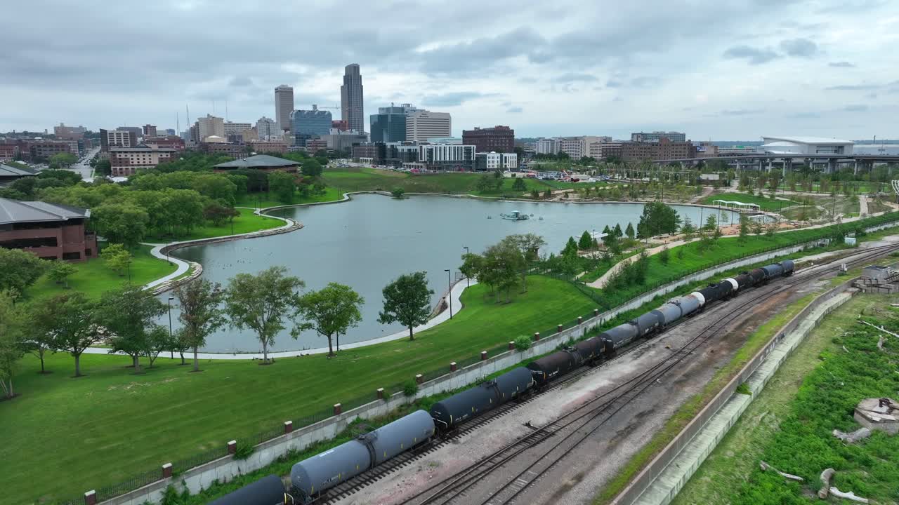 Aerial view of Omaha's waterfront, showcasing a train track, city skyline, and riverbank greenery
