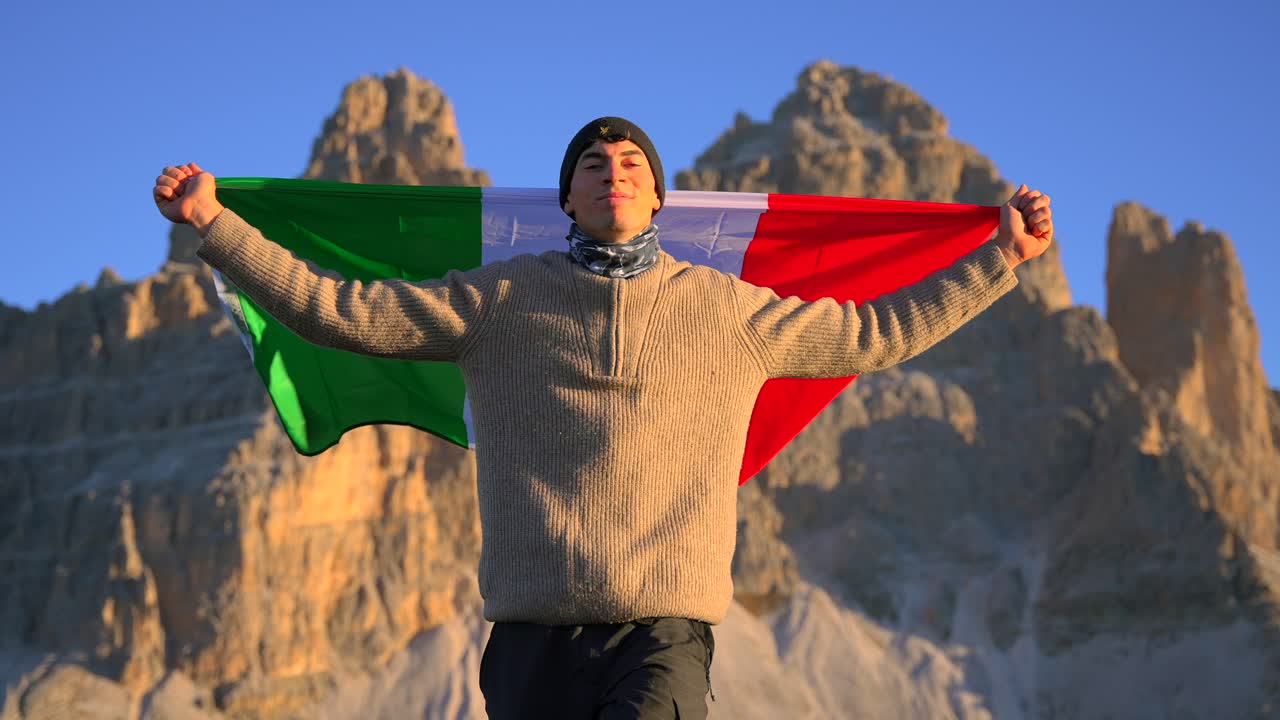 imágenes filmadas en rifugio auronzo, tri cine en las montañas de los dolomitas italianos con un hombre moviéndose y sosteniendo una bandera italiana y con hermosas montañas en el fondo, filmadas al amanecer en 4k