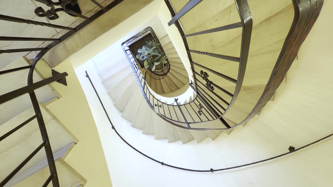 Una vista rotante verso il basso segue l'elegante spirale di una scala storica, rivelando ringhiere in ferro battuto ornate, gradini in pietra naturale. Ripresa aerea rotante