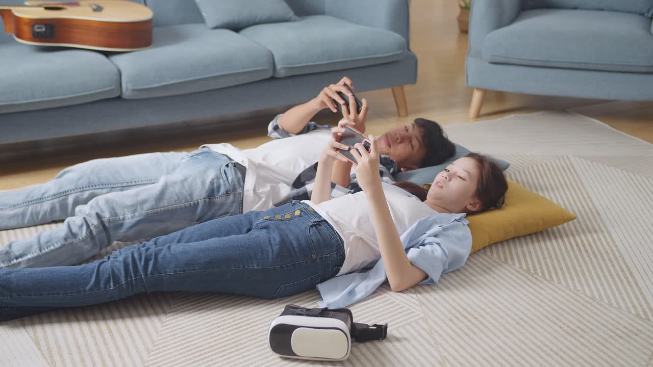 아시아 십대 부부는 집에서 바닥에 카에 누워 스마트폰으로 게임을 즐긴다.