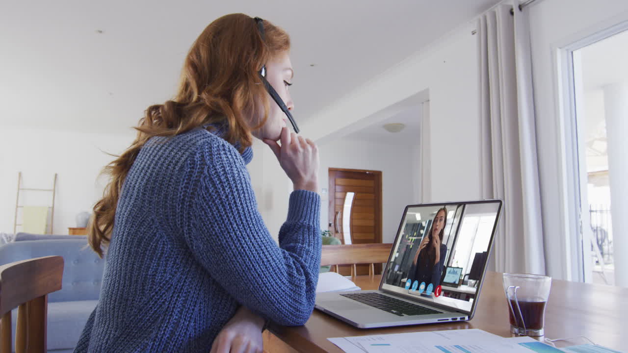 mujer caucásica con auriculares de teléfono haciendo una videollamada con una colega en una computadora portátil en casa