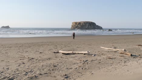 a man with long red hair runs towards the camera on a sandy beach in oregon