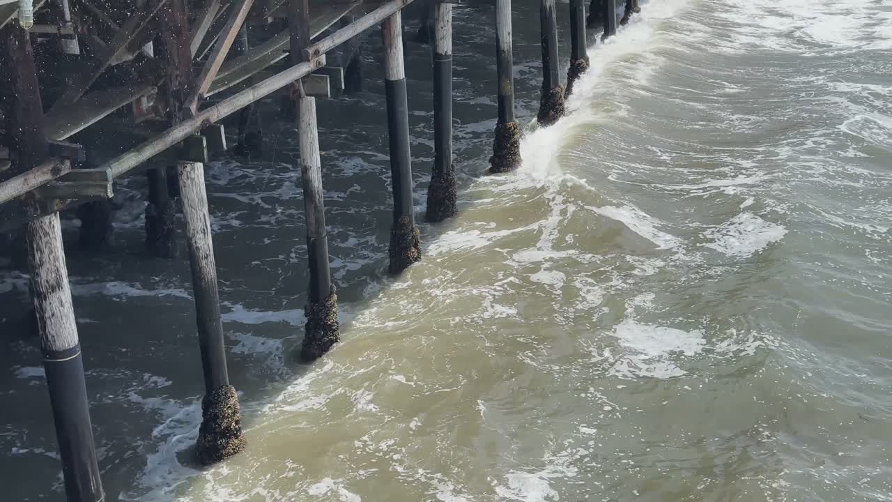 Closer view about the part of Santa Monica Pier supports where foamy waves crashing underneath, Los Angeles, USA.