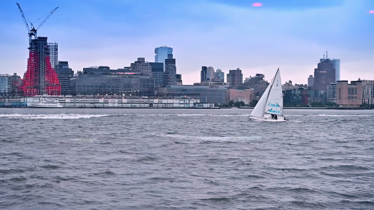 A sailboat moves by the Hudson River in New York, USA. Sailing sport in American metropolis on a gloomy day