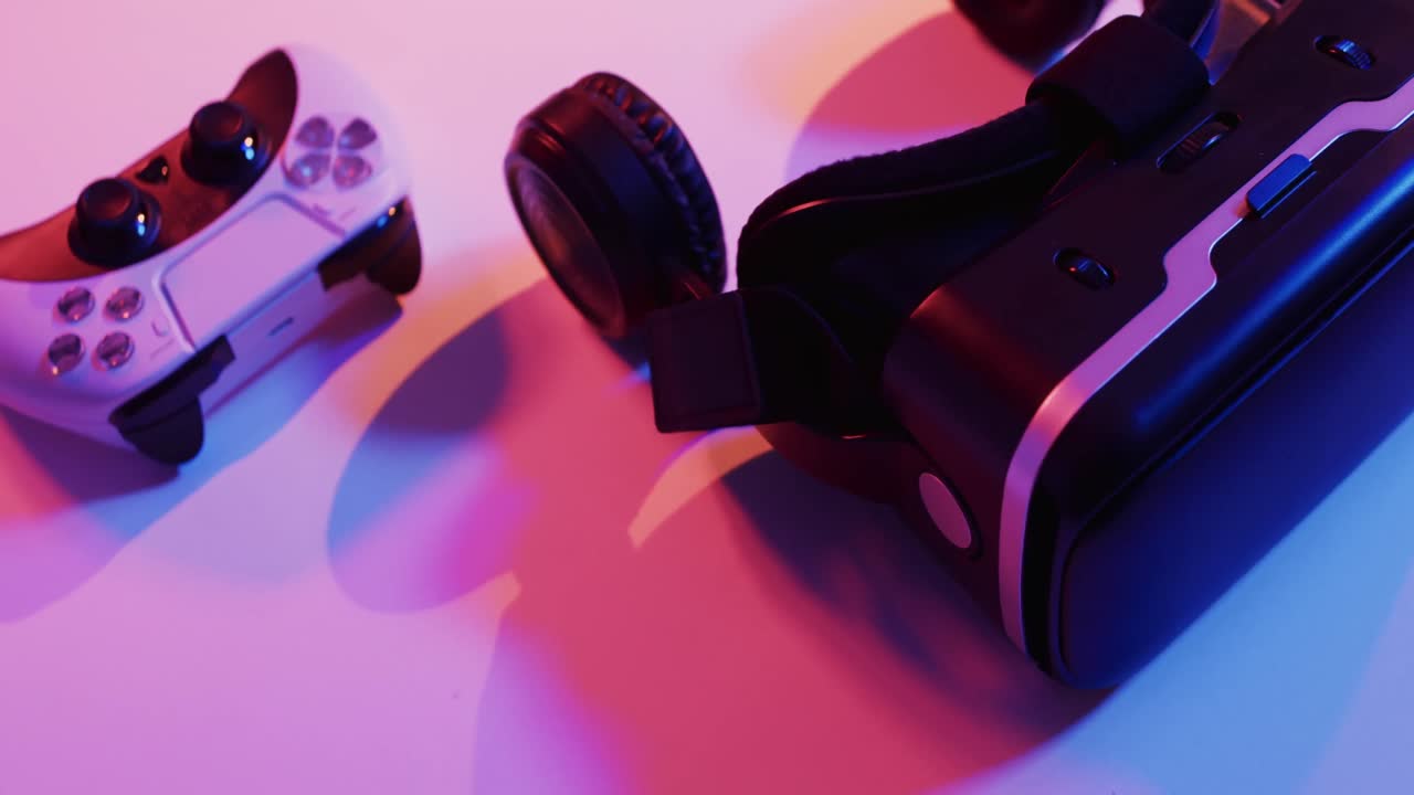 Video of close up of video game pad controller and vr headset with copy space on neon background