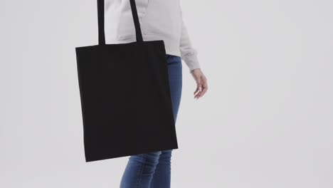 caucasian woman wearing white hoodie holding black bag on white background, copy space, slow motion