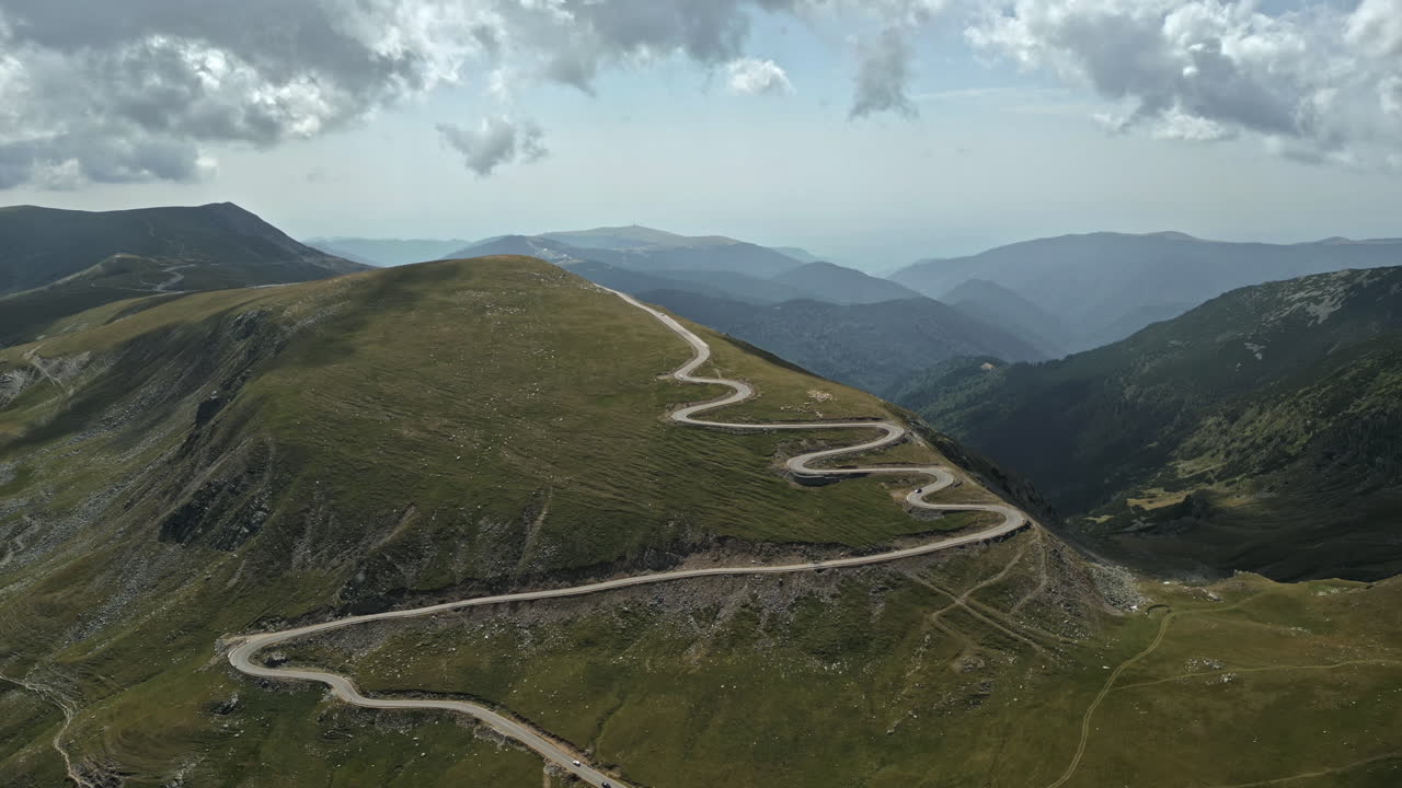 Breathtaking aerial view of Romania's Transalpina road, weaving through majestic green mountains under a clouded sky