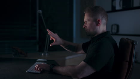 man works alone at night in dimly lit office with glow from monitor on his face, motions to zoom in, overlay ready