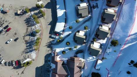 High drone shot of Big Sky Montana condos in a snow-covered mountain town, with frozen roads, smoke rising from chimneys, and peaceful woods surrounding this idyllic alpine retreat