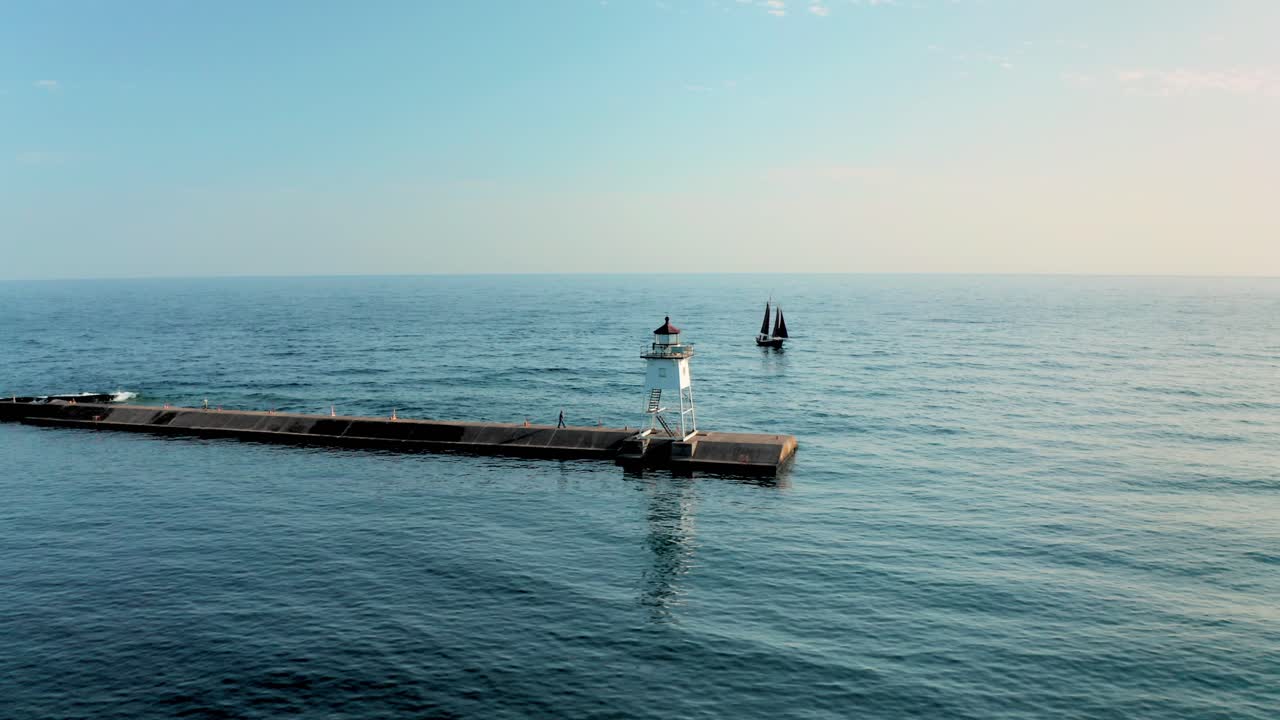 작은 흰색 등대와 슈피리어 호수의 물 위에 떠 있는 범선의 공중 궤도 전망