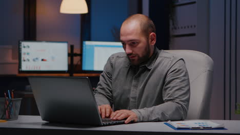 overworked businessman rubbing face while working at financial statistics