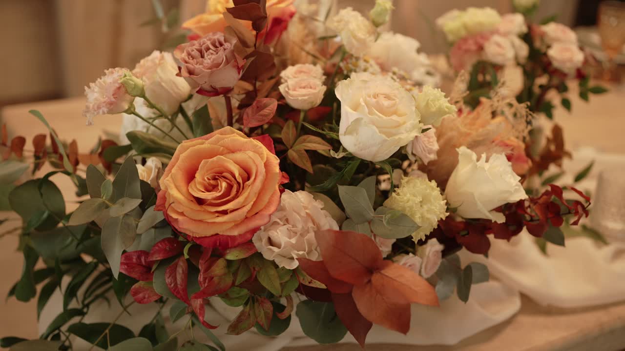 Nærbillede af et bryllupsblomsterarrangement med roser og grønt på et bord