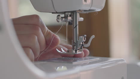 una costurera inserta el hilo en la aguja de una máquina de coser - toma de primer plano