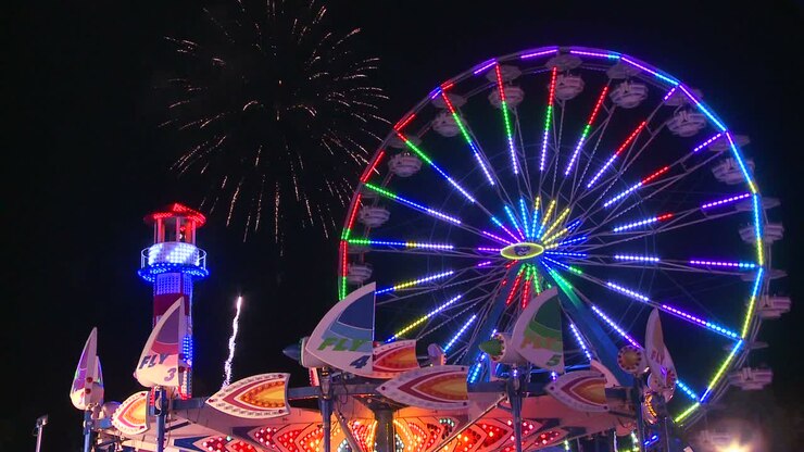 Fireworks explode in the night sky behind a ferris wheel at a carnival or state fair 2