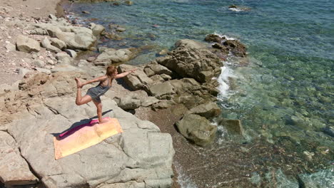 bella mujer mantiene la posición de yoga en una roca junto al mar en cerdeña, italia - zoom aéreo de drones en cámara lenta