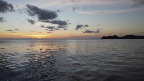 aerial: drone is traveling super low and than gains the altitude above the coastal waves on the sunset with islands on the background
