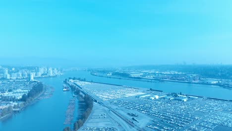 car dealership vehicle storage 4k drone flyover island filled in rows overlooking new westminster port of trade dock for import export lot on a sunny day in vancouver bc canada logs floating on river