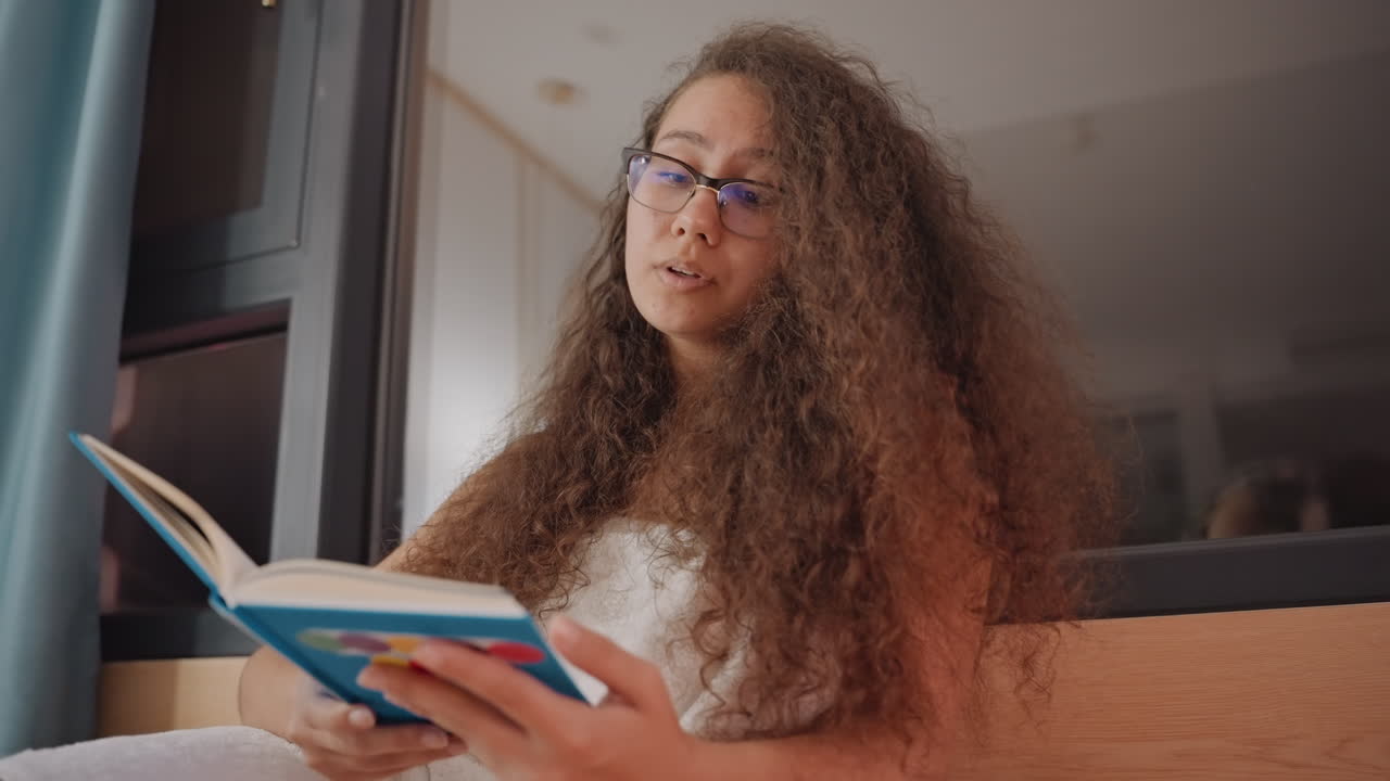 Femme s'engageant pensivement avec son journal. Femme lisant et écrivant calmement dans un environnement de chambre d'hôtel. Étudiante étudie et réfléchit avec son journal et des lunettes près d'un coin fenêtre douillet.