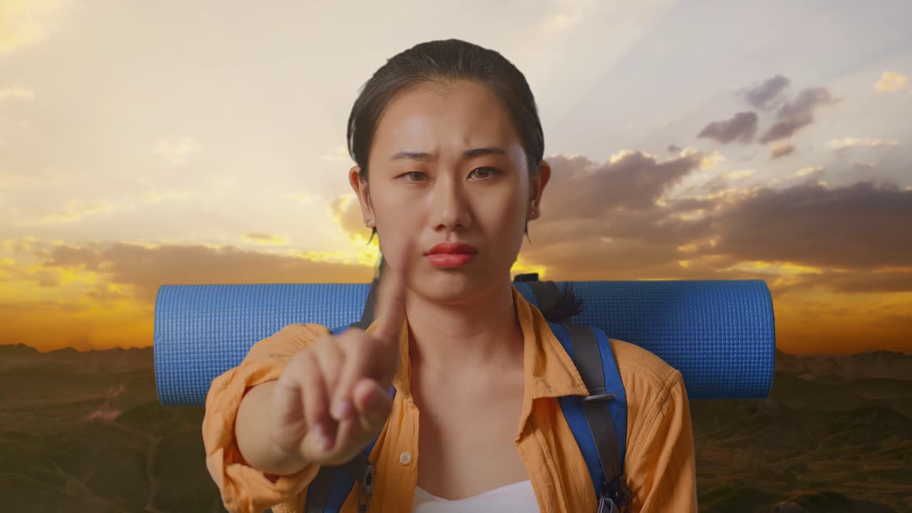 Close Up Of Asian Female Hiker With Mountaineering Backpack Showing No Gesture With Index Finger While Standing On The Top Of Mountain During Sunset Time