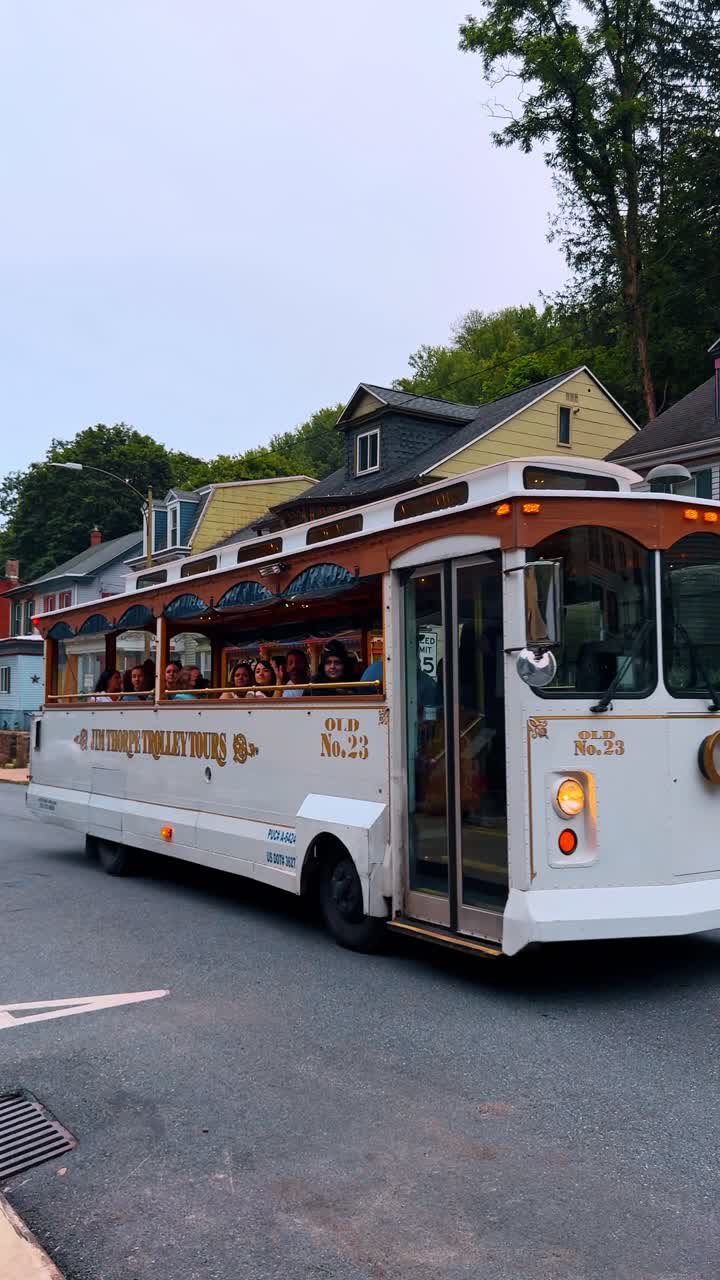 Jim Thorpe, USA, 2 July 2025: White vintage tourist trolley driving on asphalt road. A white and brown sightseeing trolley bus transporting passengers through a historic mountain town street