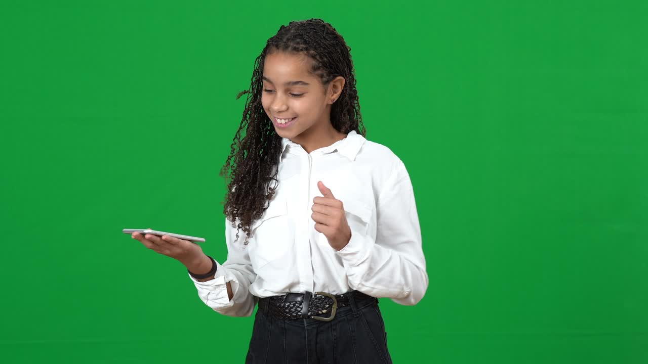 Relaxed teen girl tapping finger on smartphone touchscreen smiling on green screen. Surprised African American teenager with futuristic modern technology at chromakey background.