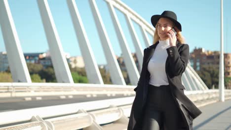 young woman talking on mobile phone on bridge in sunlight