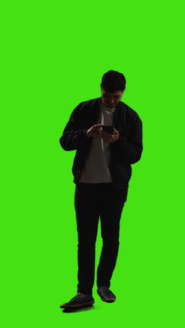 video vertical de larga duración de un joven que envía mensajes de texto en un teléfono móvil de pie contra la pantalla verde 4