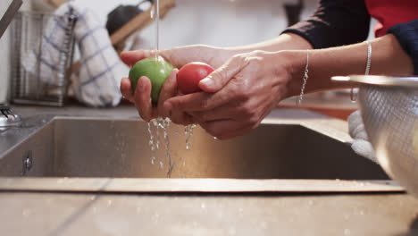 las manos de una mujer biracial enjuagando verduras en la cocina, en cámara lenta.