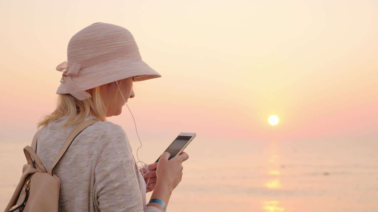 ni un minuto sin teléfono la chica está parada en la playa con un cielo rosa y el cielo mirando th