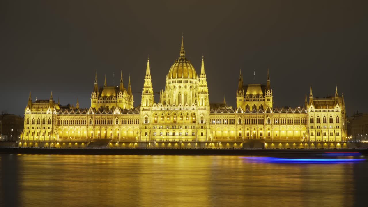 Time-lapse of the illuminated Hungarian Parliament building at night, viewed across the Danube River with light snowfall, showcasing Budapest's iconic architecture and scenic winter cityscape