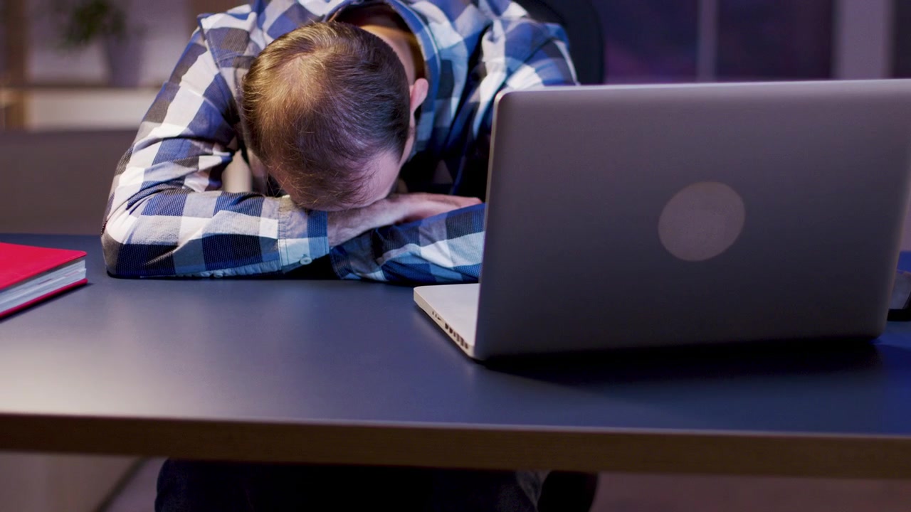 Exhausted Man Sleeping at Desk with Laptop in Office