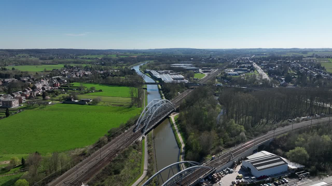 Aerial zoom in showing railway bridges crossing canal in Brussels region, Belgium, with countryside and urban areas