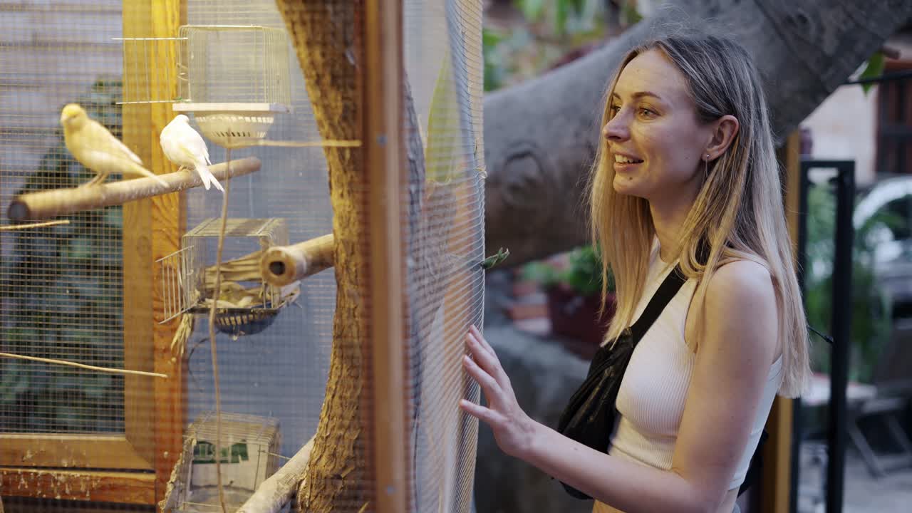 Donna sorridente che guarda un uccello in gabbia, all'aperto.