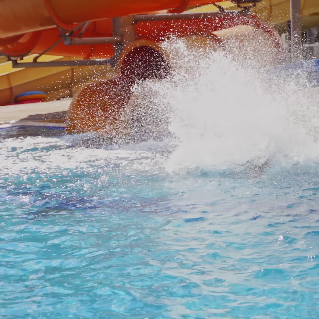 Colorful slides in the outdoor aqua park. Happy boy sliding down from slide into the swimming pool in summer. Slow motion.