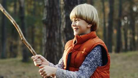 close-up view of cute caucasian blond boy playing with a stick in the forest cheerfully