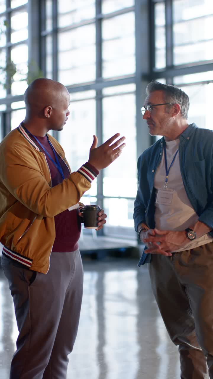 Vertical video: Man with coffee cup raising hand as colleague arriving for discussion in lobby