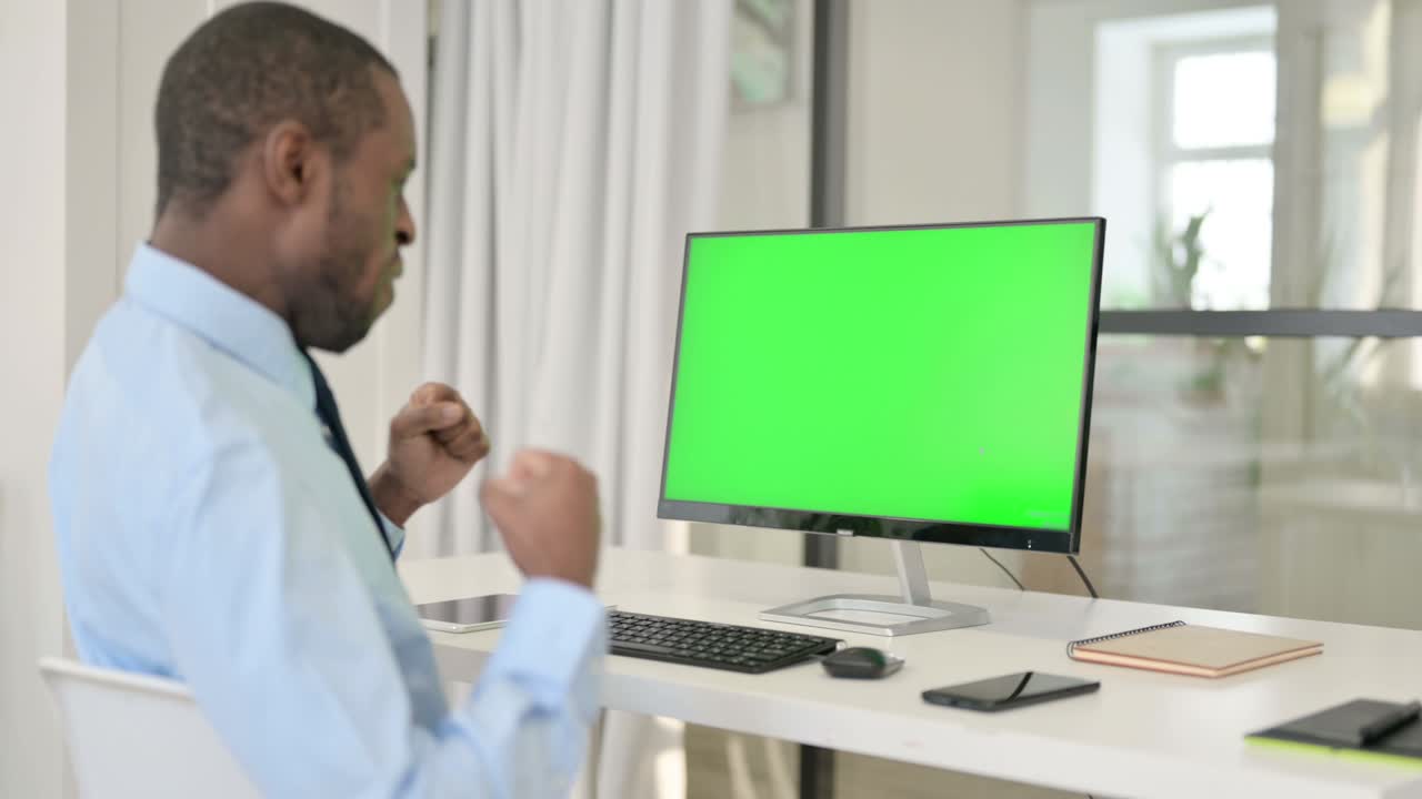 Uomo d'affari che festeggia mentre usa un desktop con schermo verde chroma key.