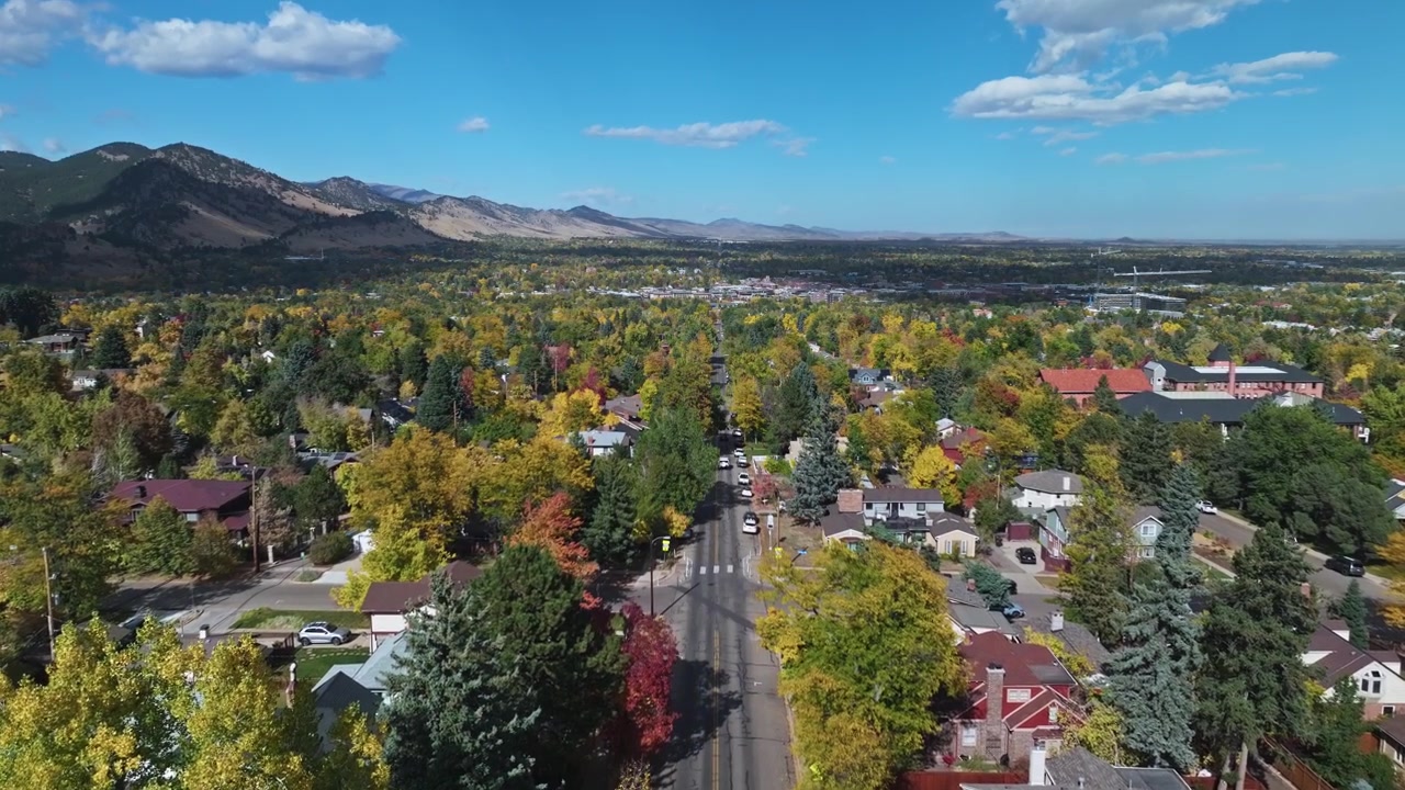 Vista aérea de um subúrbio de Boulder, Colorado, com paisagem outonal em um dia ensolarado, os icônicos Flatirons e áreas vibrantes cercadas por folhagem.