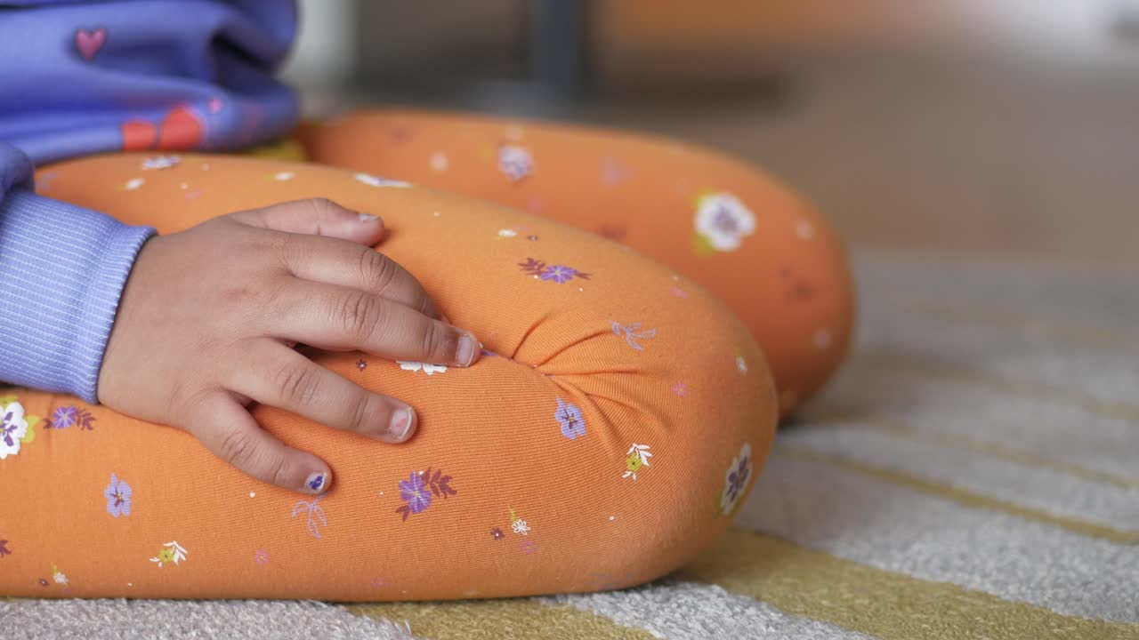 una niña sentada en el suelo con las piernas cruzadas.