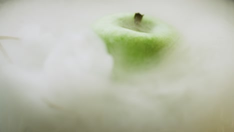 an apple with mist over it sits in straw as it rotates in a studio