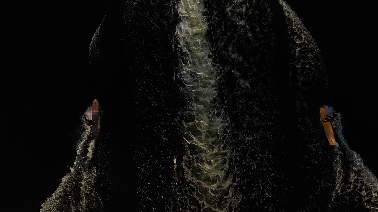 dos surfistas en longboard surfeando en ola detrás de un bote filmado con drones