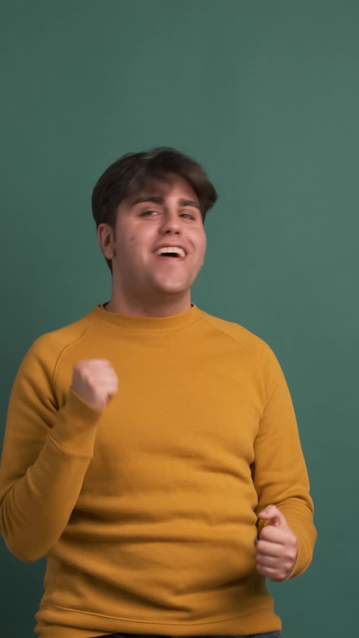 Hispanic young man dancing cheerful on green background