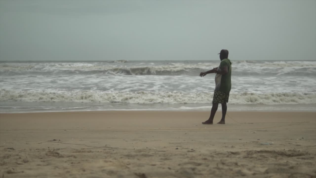 해변에서 낚시를 하고 바다 파도에서 물고기를 잡기 위해 끈을 끄는 남자