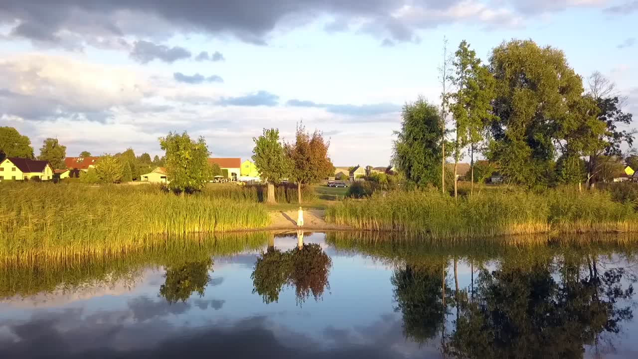 vuelo aéreo de 1 millón de dólares de una chica vestida de rosa caminando en una playa de lago al atardecer de verano en un lago y reflejando en el agua en brandeburgo, alemania