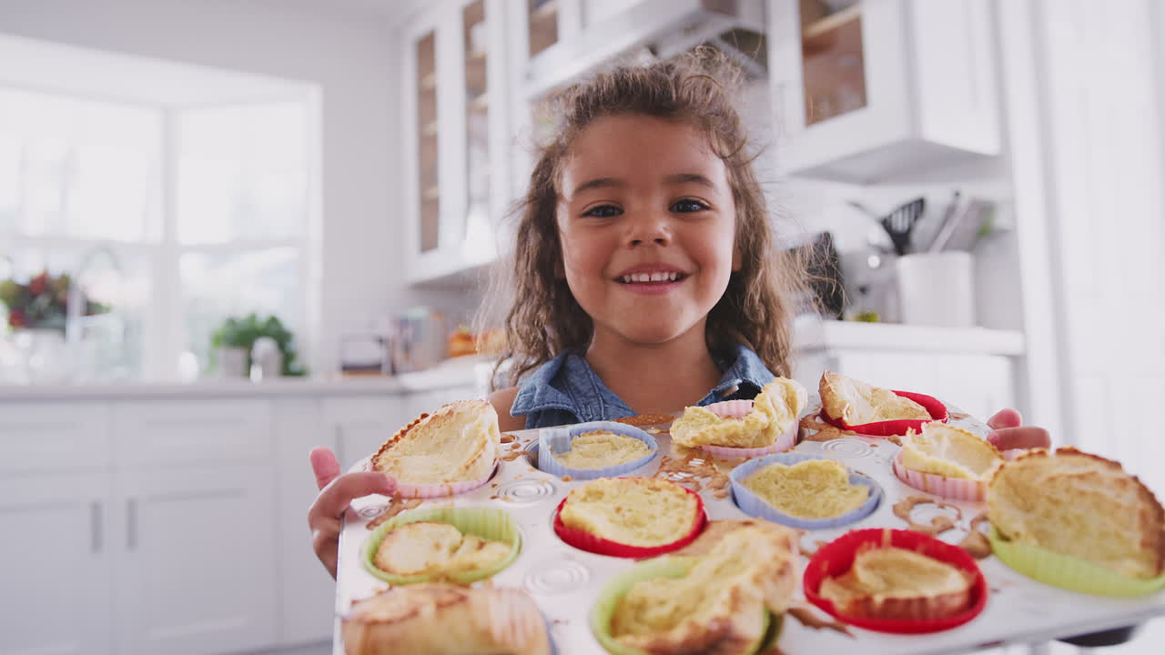 Giovane ragazza ispanica felice in piedi in cucina che presenta alla telecamera le torte che ha preparato, primo piano.